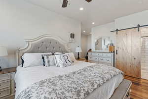 Bedroom with ceiling fan, a barn door, and light wood-type flooring