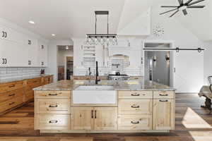 Kitchen with light stone counters, ceiling fan, a barn door, and an island with sink