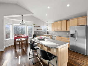 Kitchen with appliances with stainless steel finishes, a center island, pendant lighting, and light brown cabinetry