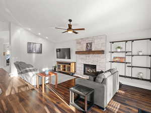 Living room featuring dark wood-type flooring, ceiling fan, lofted ceiling, and a fireplace