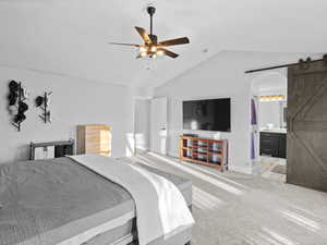 Bedroom with ensuite bath, light colored carpet, vaulted ceiling, ceiling fan, and a barn door