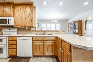 Kitchen featuring sink, white appliances, kitchen peninsula, a textured ceiling, and an inviting chandelier