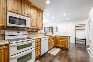 Kitchen with dark wood-type flooring, sink, kitchen peninsula, white appliances, and backsplash