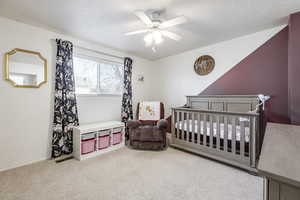 Bedroom with a crib, ceiling fan, carpet, and a textured ceiling