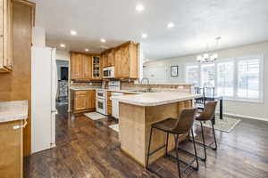 Kitchen featuring tasteful backsplash, sink, a kitchen breakfast bar, hanging light fixtures, and white appliances