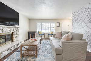 Living room with a stone fireplace, dark wood-type flooring, and a textured ceiling