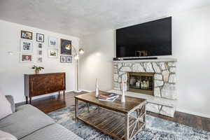 Living room featuring a stone fireplace, a textured ceiling, and dark hardwood / wood-style flooring