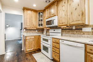 Kitchen with tasteful backsplash, white appliances, dark hardwood / wood-style flooring, and light stone counters