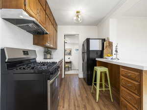 Kitchen with gas stove, black refrigerator, ornamental molding, dark hardwood / wood-style flooring, and decorative backsplash