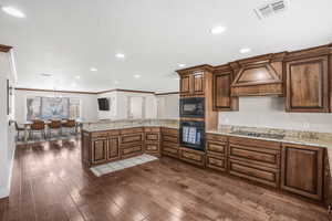 Kitchen with dark wood-type flooring, hanging light fixtures, black appliances, custom exhaust hood, and kitchen peninsula