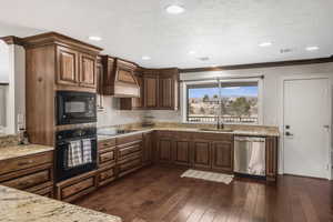 Kitchen with premium range hood, dark hardwood / wood-style floors, sink, black appliances, and a textured ceiling