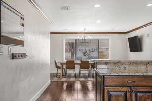 Interior space with light stone counters, dark wood-type flooring, ornamental molding, and a chandelier