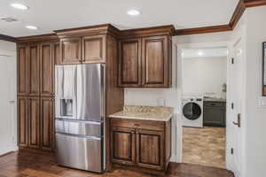 Kitchen with washer / clothes dryer, crown molding, light stone countertops, and stainless steel refrigerator with ice dispenser