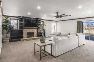 Carpeted living room featuring crown molding, ceiling fan, a stone fireplace, and a healthy amount of sunlight