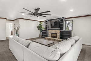 Living room featuring ornamental molding, a stone fireplace, and dark carpet