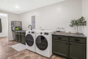 Clothes washing area featuring cabinets, electric panel, washer and clothes dryer, and sink