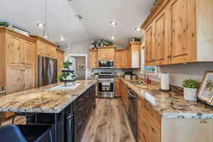 Kitchen featuring sink, light stone counters, appliances with stainless steel finishes, a kitchen island, and pendant lighting