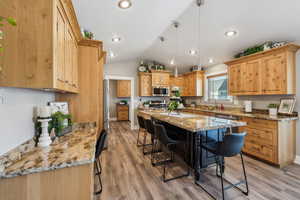 Kitchen with a breakfast bar area, light stone counters, light wood-type flooring, pendant lighting, and stainless steel appliances