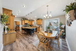 Dining space featuring an inviting chandelier, sink, vaulted ceiling, and light hardwood / wood-style floors