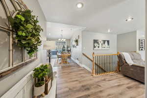 Hall with lofted ceiling, light hardwood / wood-style floors, and a notable chandelier