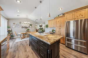 Kitchen with hanging light fixtures, stainless steel appliances, a center island, light stone counters, and vaulted ceiling