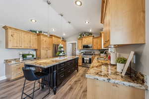 Kitchen with sink, appliances with stainless steel finishes, hanging light fixtures, a center island, and light stone countertops