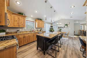 Kitchen featuring vaulted ceiling, a kitchen island, pendant lighting, and light stone counters