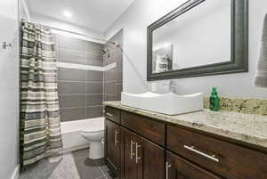 Full bathroom with vanity, tile patterned floors, shower / bath combination with curtain, and toilet