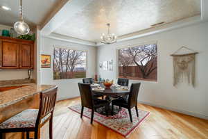 Dining area with an inviting chandelier, a tray ceiling, light hardwood / wood-style flooring, and a textured ceiling