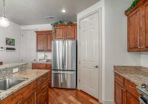 Kitchen featuring light stone counters, decorative light fixtures, light hardwood / wood-style flooring, and stainless steel appliances