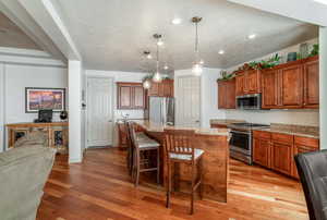 Kitchen with a breakfast bar area, decorative light fixtures, an island with sink, stainless steel appliances, and light stone countertops