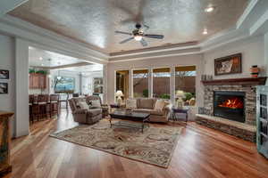 Living room featuring a raised ceiling, light wood-type flooring, a textured ceiling, and a fireplace