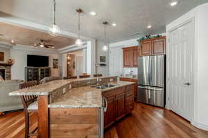 Kitchen with sink, dark wood-type flooring, stainless steel refrigerator, a breakfast bar, and a center island with sink