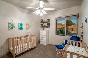 Carpeted bedroom with ceiling fan and a crib