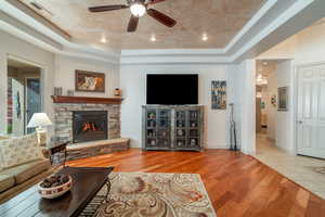 Living room featuring a raised ceiling, ceiling fan, a fireplace, and light hardwood / wood-style flooring