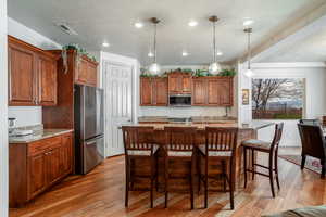 Kitchen with light stone counters, a center island with sink, appliances with stainless steel finishes, pendant lighting, and light hardwood / wood-style floors