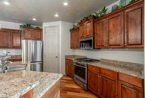 Kitchen with appliances with stainless steel finishes, sink, light stone countertops, a textured ceiling, and light hardwood / wood-style flooring