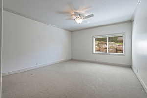 Carpeted empty room featuring ornamental molding and ceiling fan