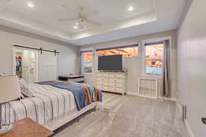 Bedroom featuring ceiling fan, a barn door, a raised ceiling, and light colored carpet