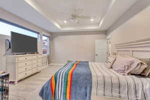 Carpeted bedroom featuring ceiling fan and a tray ceiling, and big windows