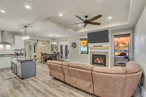 Living room with a raised ceiling, a barn door, sink, and light wood-style flooring