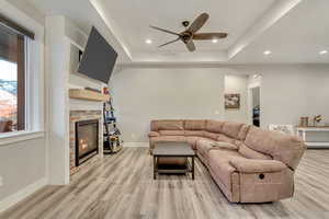 Living room featuring ceiling fan, a raised ceiling, light hardwood / wood-style floors, and a brick fireplace