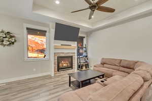 Living room with a raised ceiling, ceiling fan, a brick fireplace, and light hardwood / wood-style floors