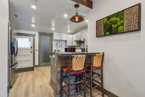 Kitchen with light hardwood / wood-style flooring, a breakfast bar area, stainless steel refrigerator with ice dispenser, white cabinets, and kitchen peninsula