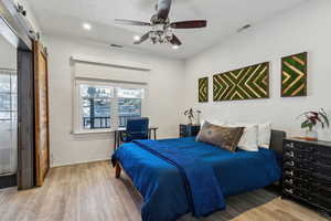 Bedroom featuring ceiling fan, wood-type flooring, and a barn door