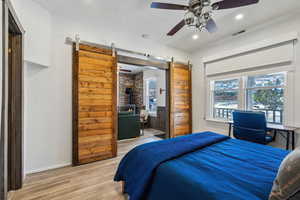 Bedroom featuring hardwood / wood-style floors, a barn door, ceiling fan, and a wood stove