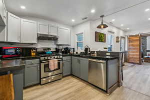 Kitchen with appliances with stainless steel finishes, decorative light fixtures, sink, kitchen peninsula, and a barn door