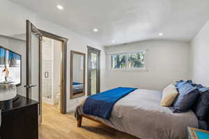 Bedroom featuring lofted ceiling, ensuite bathroom, and light wood-type flooring