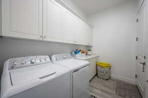 Laundry room featuring light hardwood / wood-style floors, washing machine and dryer, and cabinets