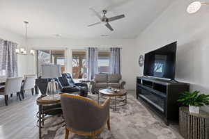 Living room with ceiling fan with notable chandelier and light hardwood / wood-style floors